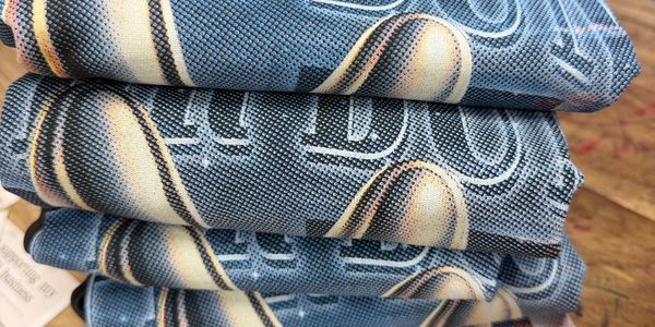 Stacked folded T-shirts on a wooden table with a thank you note.
