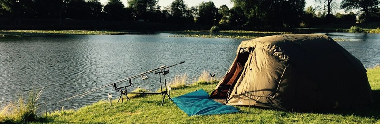 Fishing setup with tent by the lake under soft sunlight.