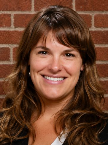 Smiling woman with wavy brown hair against a brick wall.