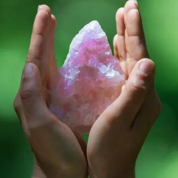 Hands holding a pink crystal.