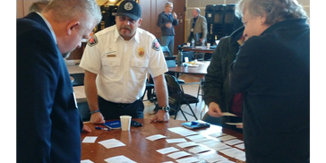 Emergency responder and community members review cards laid out on table during planning session.