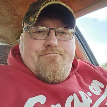 Man wearing glasses and a cap in a car, dressed in a red hoodie.