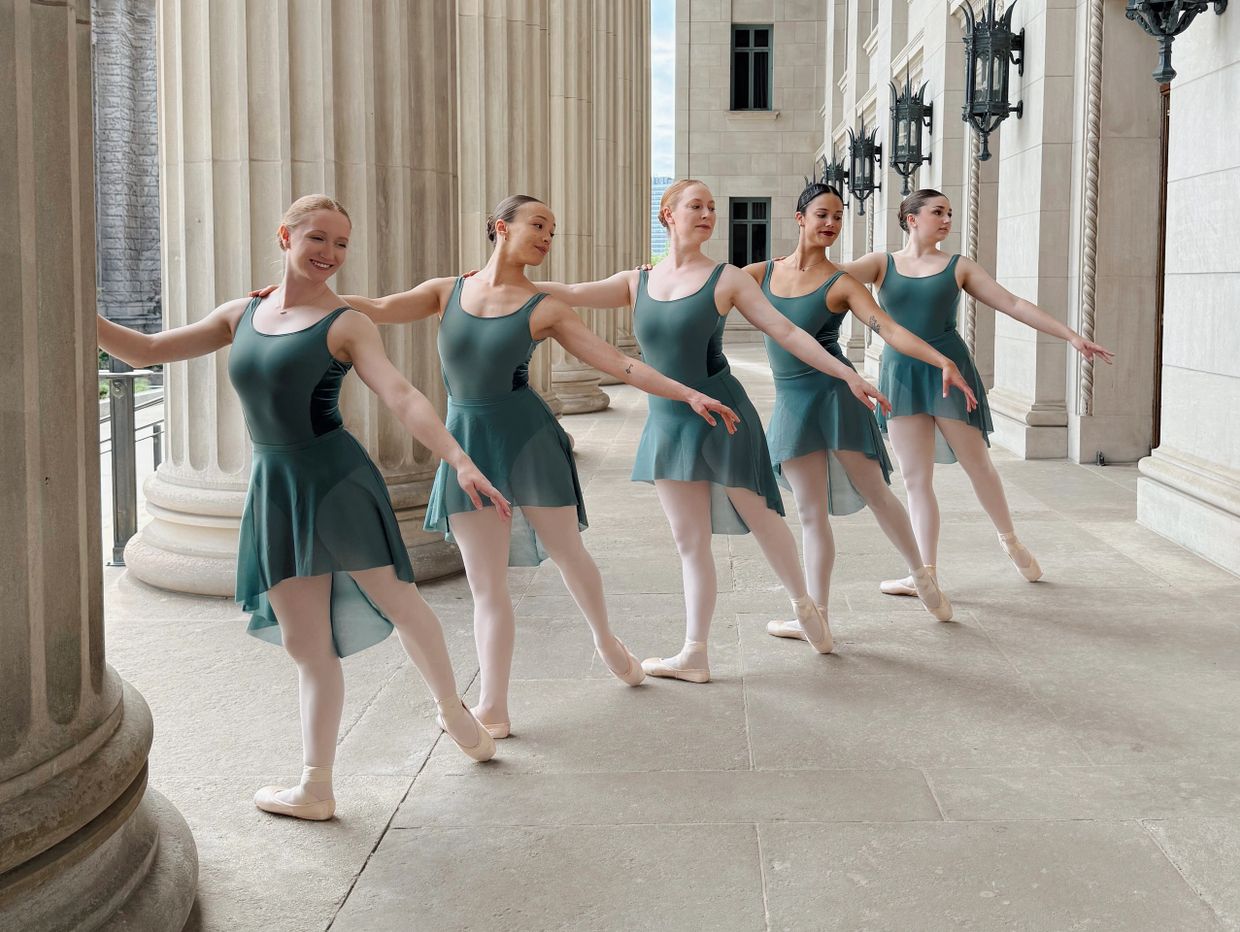Five ballerinas in teal dresses pose gracefully in a classical architectural setting.
