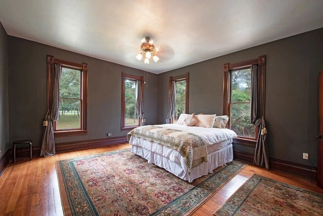 Cozy bedroom with multiple windows and vintage rugs on wooden floors.