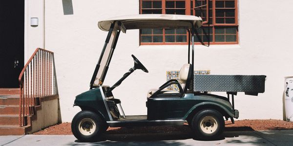 Dark green golf cart parked beside a building with a white wall.