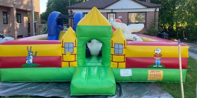 Colorful inflatable bounce house with cartoon characters outside a house.