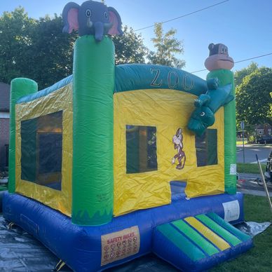 Colorful inflatable bounce house with zoo animal decorations in a sunny backyard.