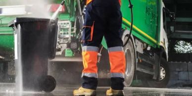 Worker cleaning a garbage bin with water pressure.