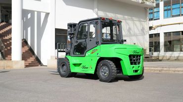 A bright green forklift parked outdoors near a building on a sunny day.