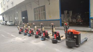 A lineup of electric pallet jacks outside an industrial warehouse.