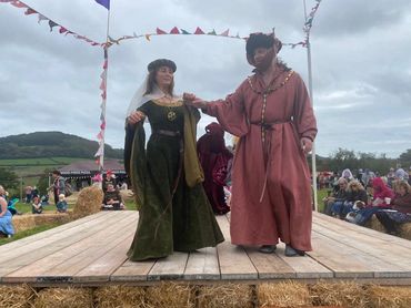 Two people in medieval costumes dancing on a wooden stage.