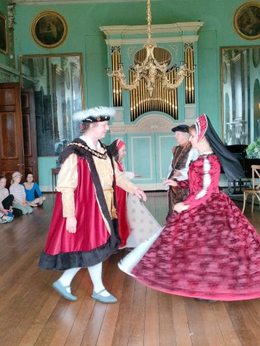 People dancing in historical costumes in a grand room.