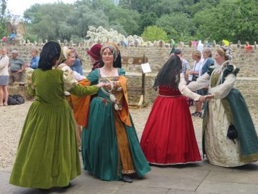 Women in medieval gowns dancing outdoors.