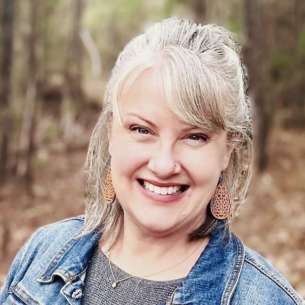 Owner Janelle James headshot, smiling with blue denim jacket on over gray sweater.