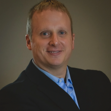 Professional man in a dark blazer and light blue shirt smiling.