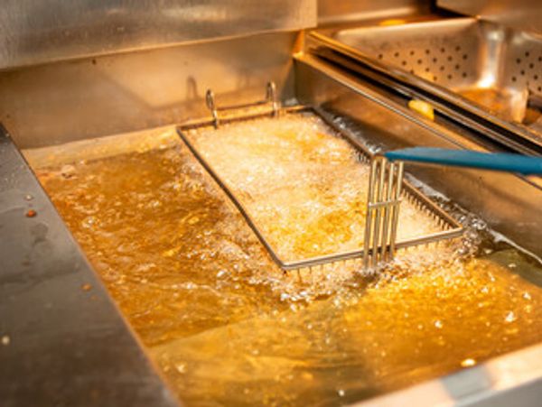 Commercial deep fryer with bubbling hot oil and a frying basket.