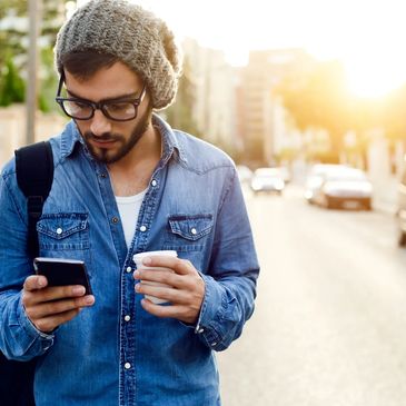 A man carrying a travel bag enjoying a coffee whilst checking his cellphone