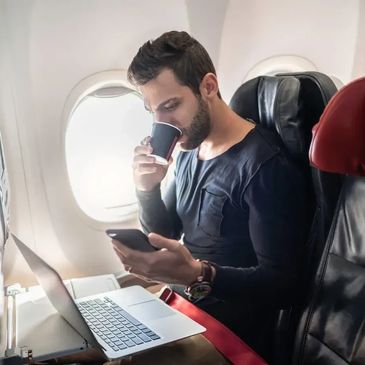 Man sitting on a plane sipping coffee whilst checking his cellphone