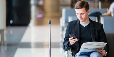 Casually dressed man sat at an airport with a carryon bag, checking his mobile phone