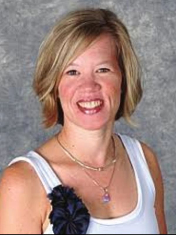 Smiling woman in white top with short blonde hair and necklace.
