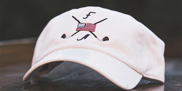 White cap with crossed golf clubs and American flag emblem.