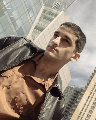 Young man in leather jacket poses against city skyscrapers.