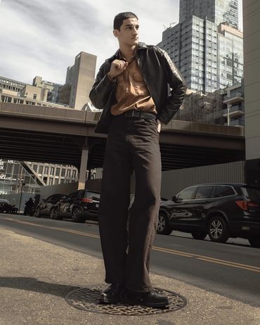Tall man in stylish outfit posing on city street with modern buildings.