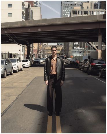 Man standing on city street under an overpass, wearing a leather jacket.