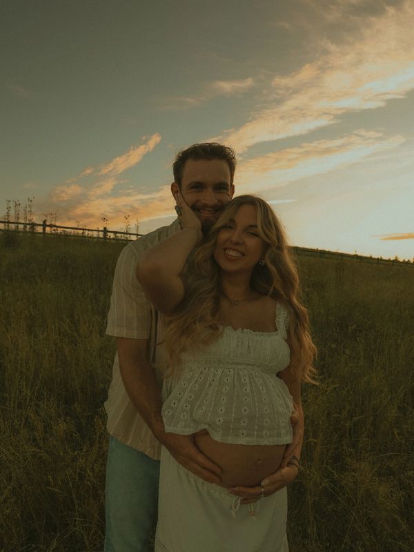 Couple embracing in a field at sunset, woman is pregnant.
