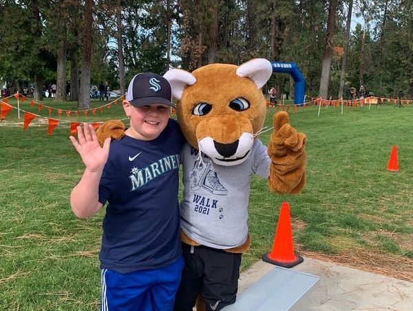 A boy poses happily with a mascot outdoors at a fun event.