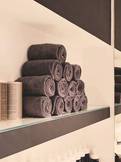 Backlit shelves display of black towels rolled and stacked neatly on white shelving w/dark trim.