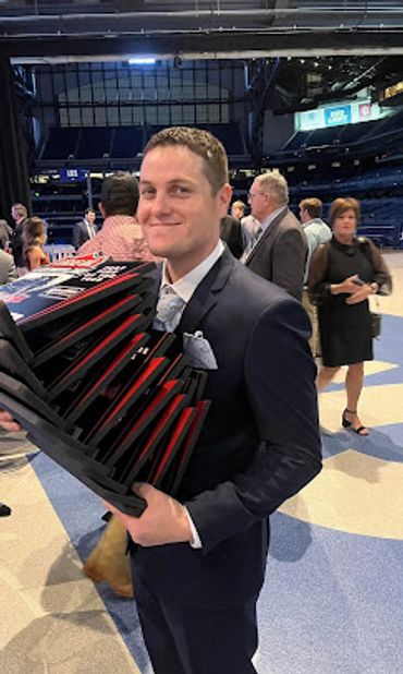 Guy in black slim fit suit with gray tie holding a huge stack of awards