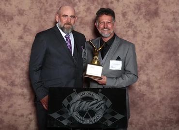 2 men in their black and grey suits accepting an award at an banquet