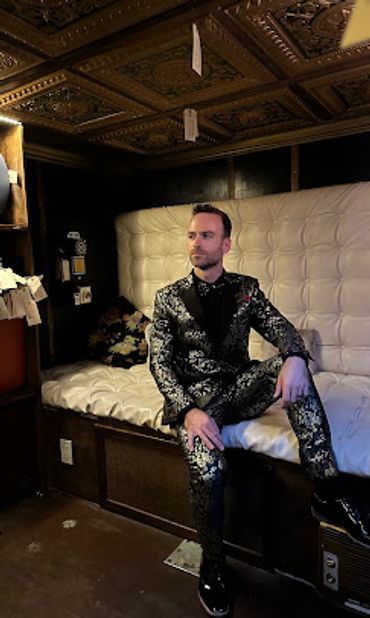 Man sitting in his high fashion floral black and gold tuxedo