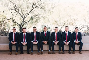 Group of groomsmen sitting around the groom in blue suits, white shirts and red ties