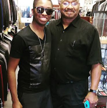 2 guys standing in the suit store with a store full of suits in the background