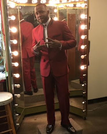 A man standing in front of a mirror in his new burgundy slim mandarin collar suit with black trim