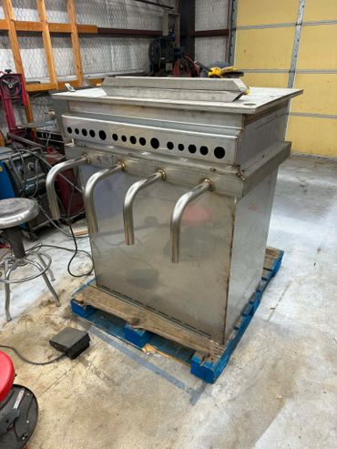 Stainless steel industrial machine with four spouts on a pallet in a workshop.