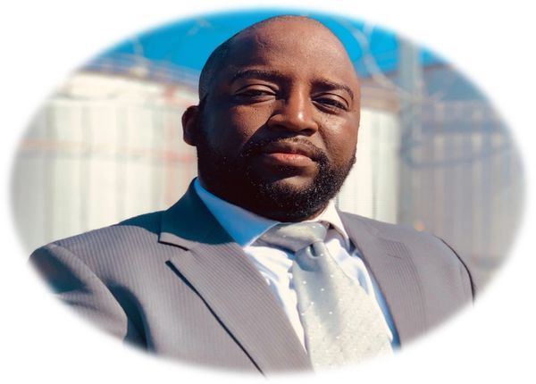 Confident man in a suit posing outdoors with a blurred background.