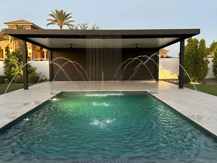 Modern backyard pool with cascading and arching water fountains under a shaded pergola.