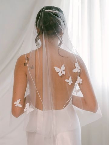 Bride with a sheer veil adorned by white butterfly appliqués on her back.