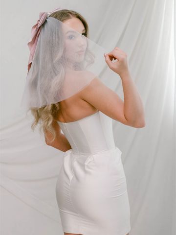 Woman in a white strapless dress with a veil and pink bow.