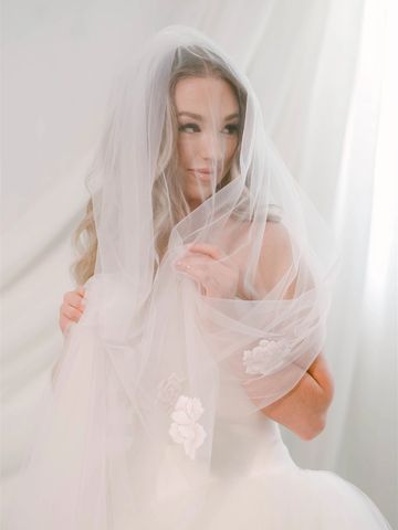 Bride wrapped in delicate white veil, softly smiling.