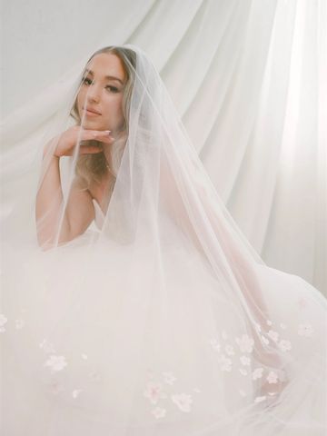 Bride in a delicate veil with floral details, posing thoughtfully.