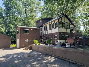 A brown two-story house surrounded by trees with an outdoor patio area.