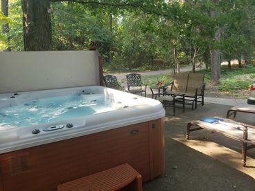 Outdoor patio with hot tub, chairs, and greenery.