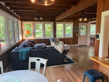 Cozy living room with wooden walls and large windows overlooking greenery.
