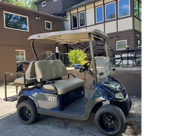 A golf cart parked outside a brown house with patio furniture.