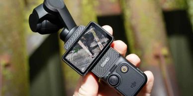 Hand holding a DJI Osmo Pocket camera with screen showing a video recording.