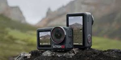 Two compact action cameras on a rock with a mountainous background.